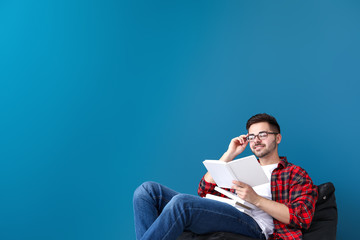 Handsome young man with books sitting near color wall