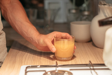 Fototapeta na wymiar Organic fruit nutrition. Cropped shot of man taking glass of orange juice in kitchen. Dark blur background.