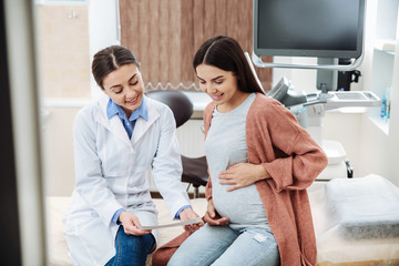 Female ultrasonographer working with pregnant woman in modern clinic