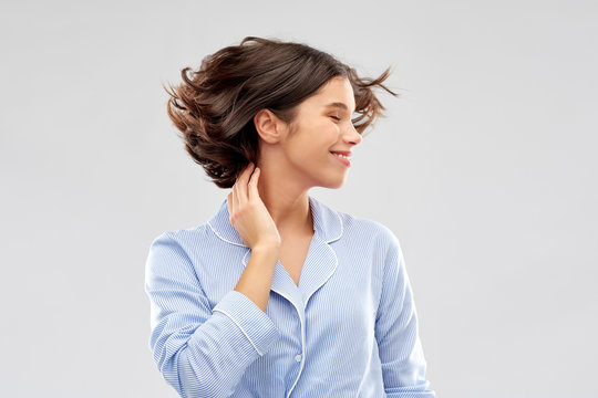 People And Bedtime Concept - Happy Young Woman In Pajama Whipping Her Hair Over Grey Background