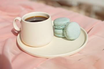 French macaroon blue plate on the pink and pink coffee cup standing on a wooden table with a pink tablecloth white vase with flowers roses and greens