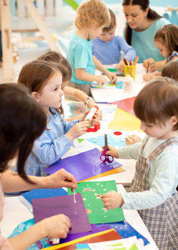 Development Learning Children In Preschool. Children's Project In Kindergarten. Group Of Kids And Teacher Cutting Paper And Gluing With Glue Stick On Art Class In Kindergarten Or Daycare