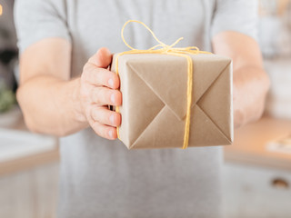Special occasion. Cropped shot of man holding rustic paper handmade gift box. Blur kitchen background.