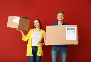 Young couple with cardboard boxes on color background