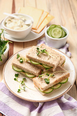 Plate with tasty cucumber sandwiches on wooden table