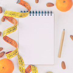 Diet concept - notebook, vintage orange yellow measuring tape, mandarins, almonds, pencil on white...