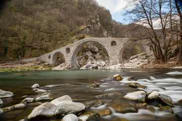 Fototapeta na wymiar Devil's bridge, Bulgaria. Ancient stone bridge over Arda river, autumn time with leaves in water. Rhodope mountain