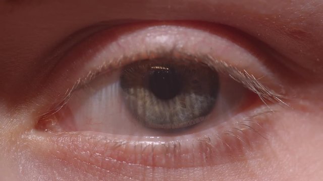 Close-up shoot of greenish eye with the reflection of lamp and person gesturing thumb-up.