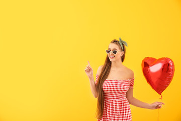 Beautiful young woman with heart-shaped air balloon on color background