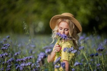 Young beautiful woman blonde in a hat walks through a field of purple flowers. Summer.