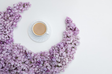 Romantic background with a cup of coffee, lilac flowers on a white table. Top view, place for text.