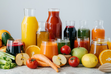Horizontal shot of squeezed vegetables and fruits in glass bottles. Set of colorful fresh apples, lemon, orange, tomatoes and celery against white background. Healthy food and drink concept.