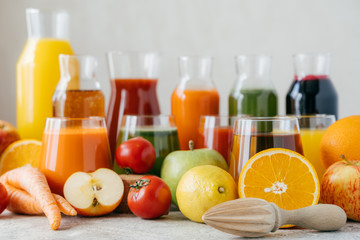 Horizontal shot of fresh fruit and vegetables on white table, glass jars of juice and orange squeezer. Healthy drinks concept. Organic beverages