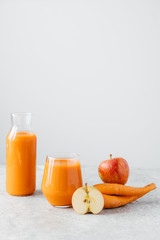 Vertical shot of fresh natural orange carrot juice in glass jar, ripe apple and carrot on white background. Healthy drink and detox.
