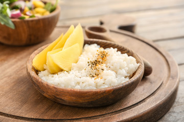 Plate with tasty rice and mango on wooden board