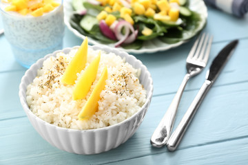Bowl with tasty rice and mango on wooden table