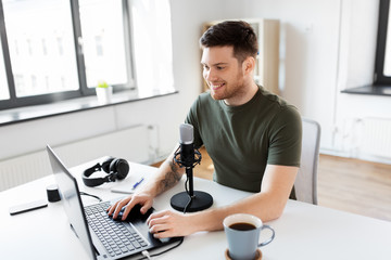 technology, mass media and podcast concept - happy young male audio blogger with laptop computer...