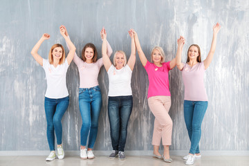 Happy women of different ages with pink ribbons near grey wall. Breast cancer concept