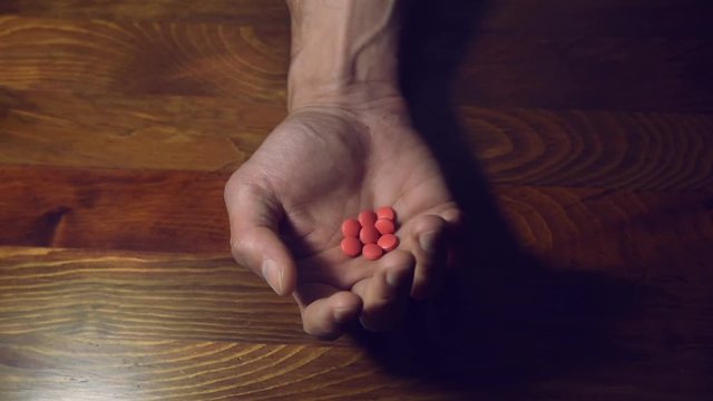 Depressed man suffering from suicidal depression want to commit suicide by taking strong medicament drugs and pills holding them in his hand and open to show them to the camera health care concept