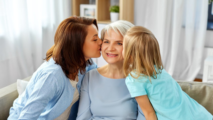 family, generation and female concept - mother and daughter kissing happy grandmother at home