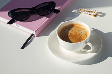 Cup, notepad and sunglasses on the white table on sunny day.