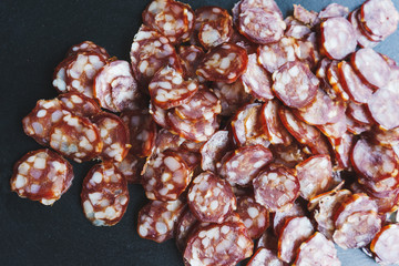 Thinly sliced sausage slices on a black stone board. 