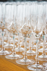 Several rows clear, clean glasses for wine and champagne on counter prepared for drinks.