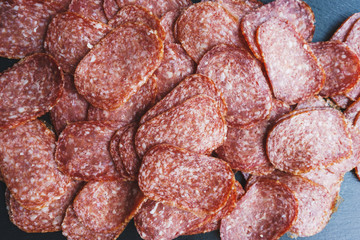 Thinly sliced sausage slices on a black stone board. 