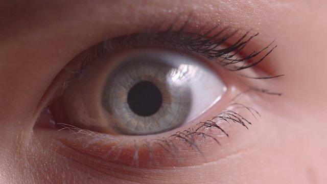 Close-up shoot of blue eye blinking with the flare on it watching downwards and into camera intently.