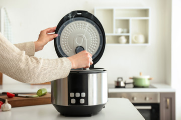 Woman cooking food in multi cooker at home