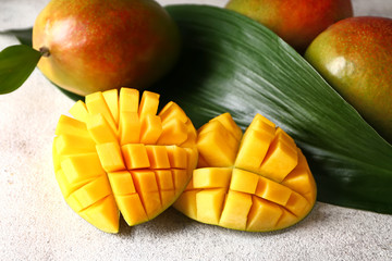 Tasty sweet mango with tropical leaf on grey background