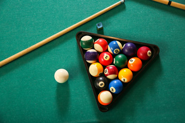 Billiard balls in triangle rack with cues on table