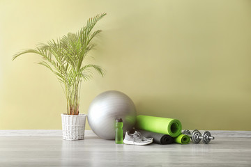 Set of sports equipment with fitness ball, bottle of water and shoes near color wall