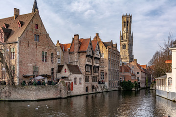 Bruges, Belgium - December 15, 2018: The Rozenhoedkaai (Quay of the Rosary) canal in Bruges with the classic medieval buildings and Belfry of Bruges in the background. Quay of Rosary in sunny day.