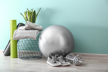 Set of sports equipment with fitness ball, towels and shoes near wall