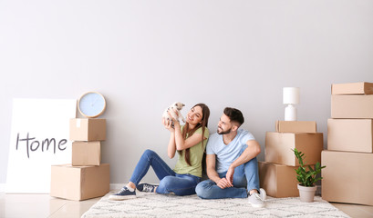 Young couple with belongings and kitten sitting near light wall in their new house