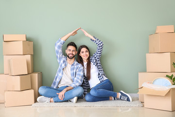 Young couple with belongings sitting near color wall in their new house