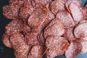 Thinly sliced sausage slices on a black stone board. 