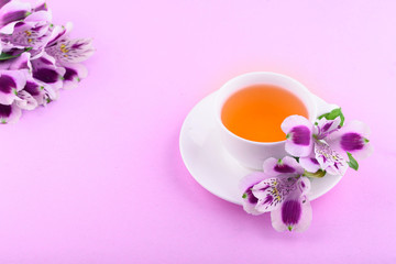 Beautiful flowers of astromeria. Herbal tea in a white cup and a white saucer on a pink background