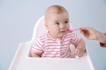 Cute little baby eating tasty food on grey background