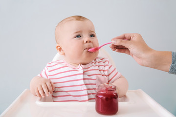 Cute little baby eating tasty food on grey background