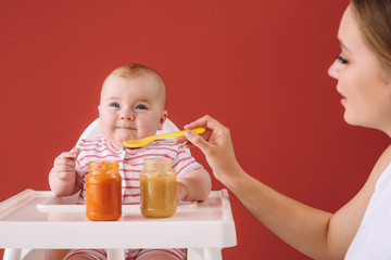 Mother feeding her little baby on color background