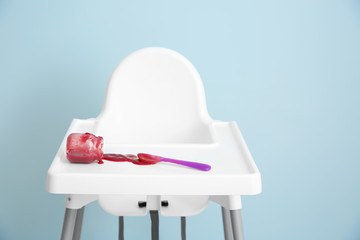 Overturned jar with tasty baby food on high chair against grey background