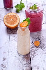 Berry and fruit smoothies in glass jars topped with mint and kumquat slices against the white wooden background