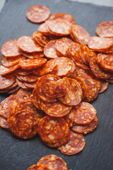 Thinly sliced sausage slices on a black stone board. 