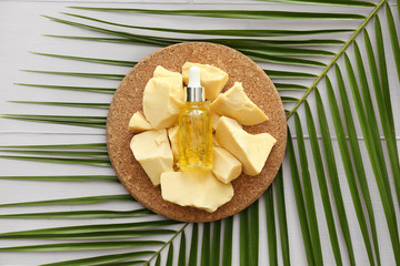 Cocoa butter, bottle of essential oil and palm leaf on table