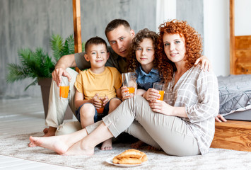 Happy family with two children drinking freshly squeezed orange juice near the bed