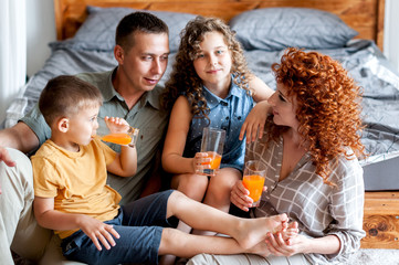 Happy family with two children drinking freshly squeezed orange juice near the bed