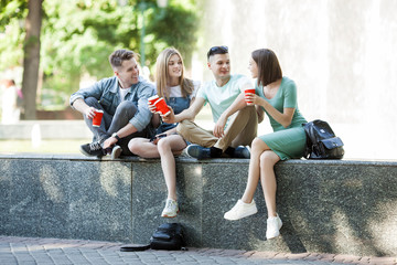 Fototapeta premium Young attractive people having fun together outdoors. People drinking coffee and smiling. Group of friends walking together.