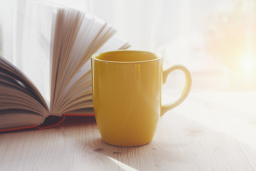 coffee cup and open book on wooden table, morning sunshine